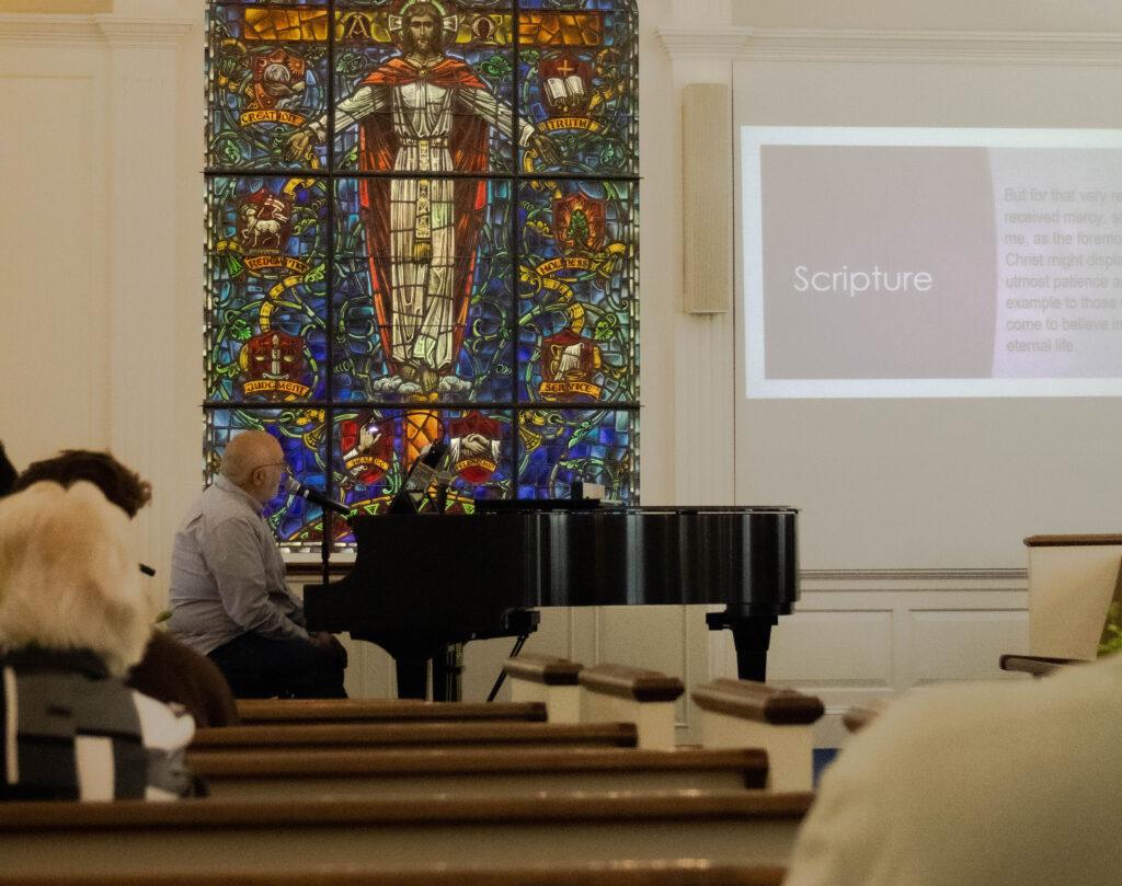 Mick Gilliam on the piano reading Scripture from a projected presentation 